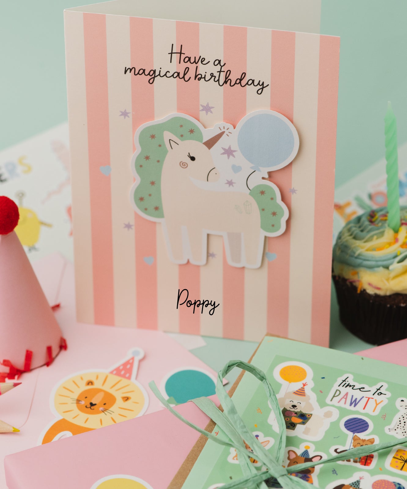 Personalised Magical Birthday Unicorn Sticker & Colouring Kids Birthday Card featuring a white unicorn with mint green mane holding a blue balloon against pink and white striped background. Card displays 'Have a magical birthday' text with scattered silver stars and personalized name.