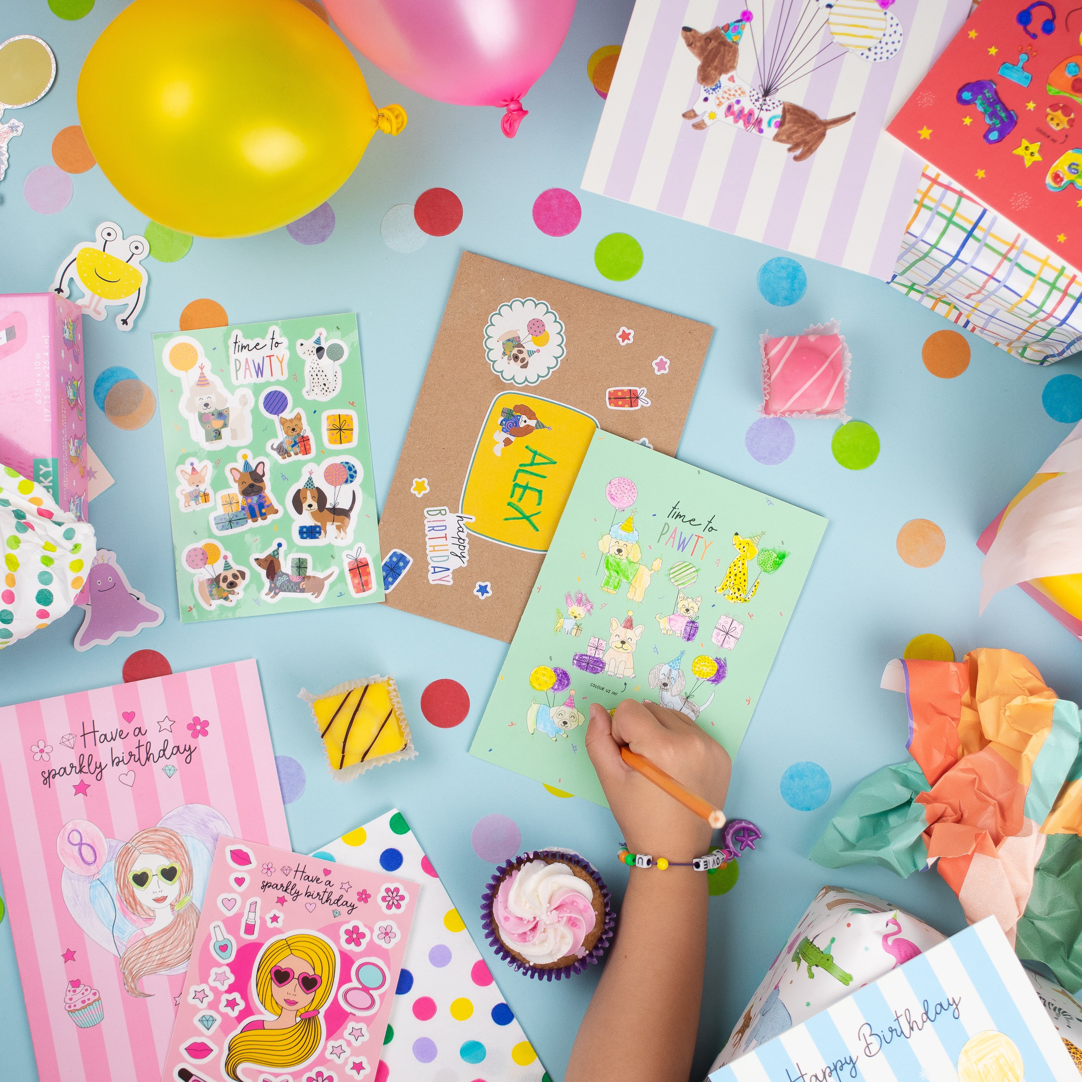 Colorful birthday party scene featuring Football Multi Sticker & Colouring Kids Birthday Card alongside festive decorations including balloons, stickers, and craft supplies on a light blue background with polka dot pattern. Decorated cards and party items spread across the surface creating a celebratory atmosphere.