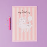 Personalised Magical Birthday Unicorn Sticker & Colouring Kids Birthday Card featuring a white unicorn illustration holding a balloon on pink striped background with silver stars, accompanied by a pink pencil and confetti on purple surface