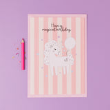 Personalised Magical Birthday Unicorn Sticker & Colouring Kids Birthday Card featuring a white unicorn illustration holding a balloon on pink striped background with silver stars, accompanied by a pink pencil and confetti on purple surface