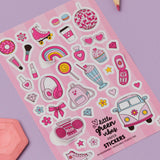Girly Dreamworld Pink Sticker Sheet featuring cute pink and white illustrations including roller skates, disco ball, headphones, rainbow, hearts, milkshake, cupcake, vintage van, and other girly icons on a pink background, displayed on purple surface with colored pencils and pink geometric shape