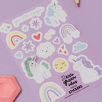 Sheet of colorful stickers with unicorns, rainbows, and hearts on a purple background.