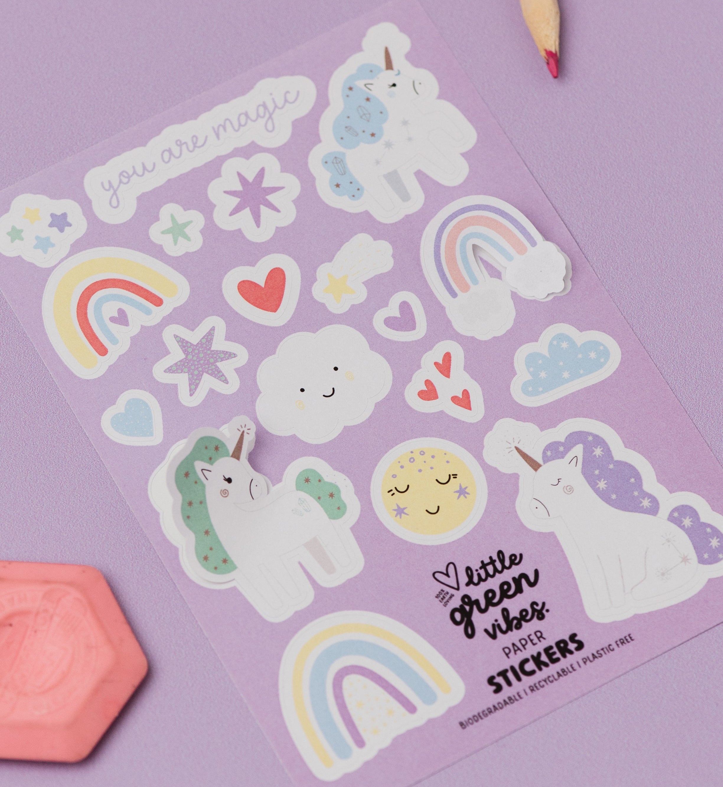 Sheet of colorful stickers with unicorns, rainbows, and hearts on a purple background.