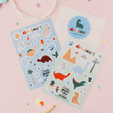 Two sheets of dinosaur stickers on a pink background with pencils and a bag.