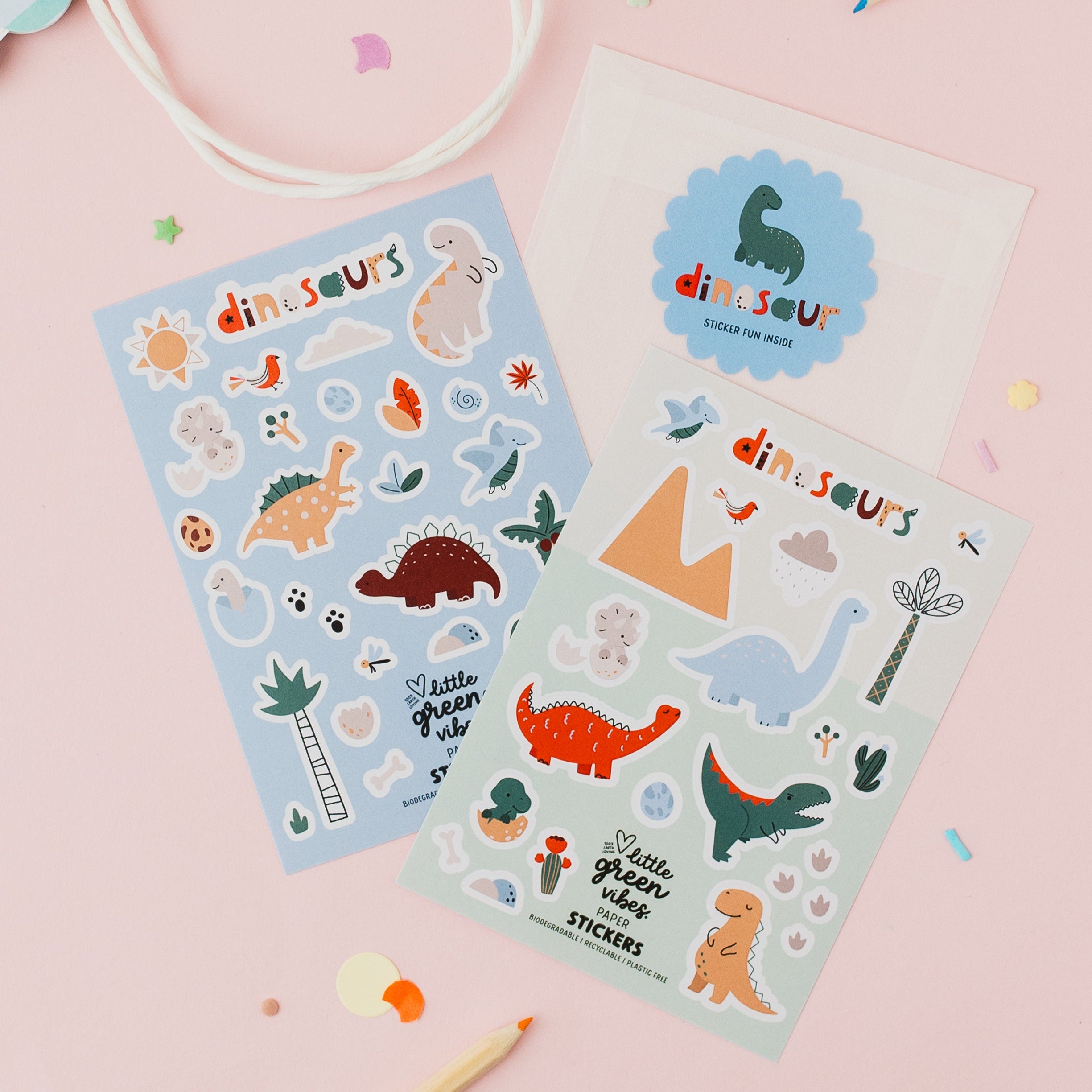 Two sheets of dinosaur stickers on a pink background with pencils and a bag.