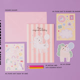 Personalised Magical Birthday Unicorn Sticker & Colouring Kids Birthday Card displayed with matching sticker sheets featuring cute unicorns, rainbows, and stars on pink striped background. Set includes coloring pencils and activity sheets arranged on purple surface.